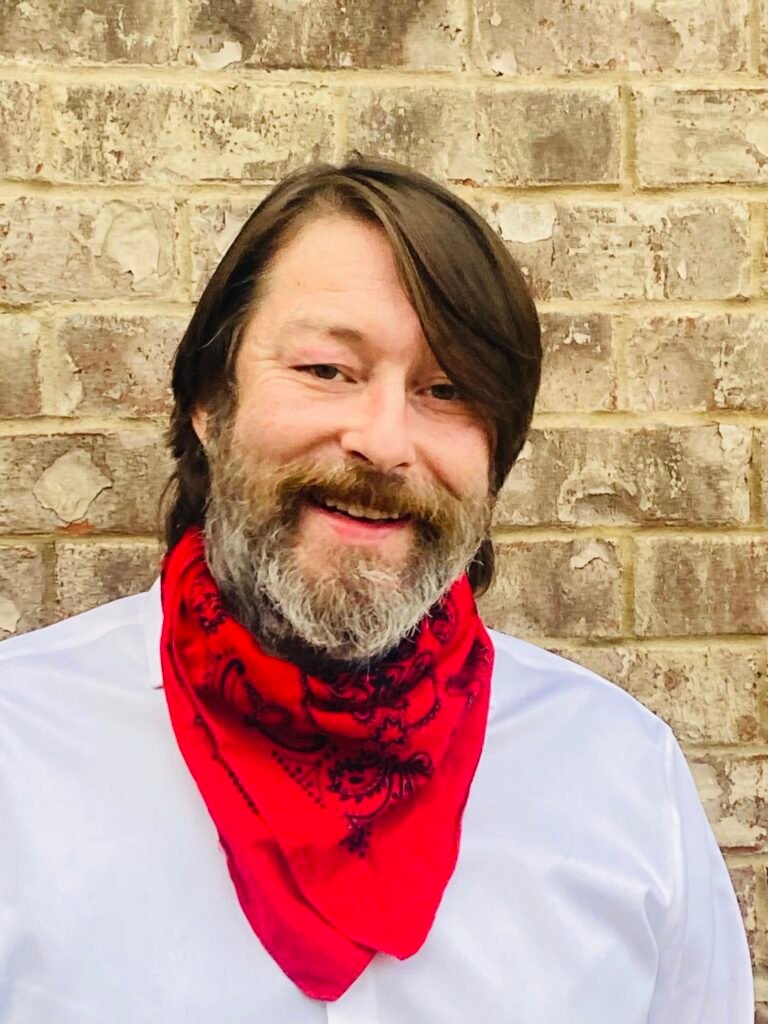 Austin Jones pictured smiling with a white button down shirt and red bandanna.